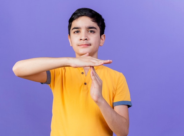 Молодой кавказский мальчик смотрит в камеру, делая жест тайм-аута, изолированный на фиолетовом фоне с копией пространства
