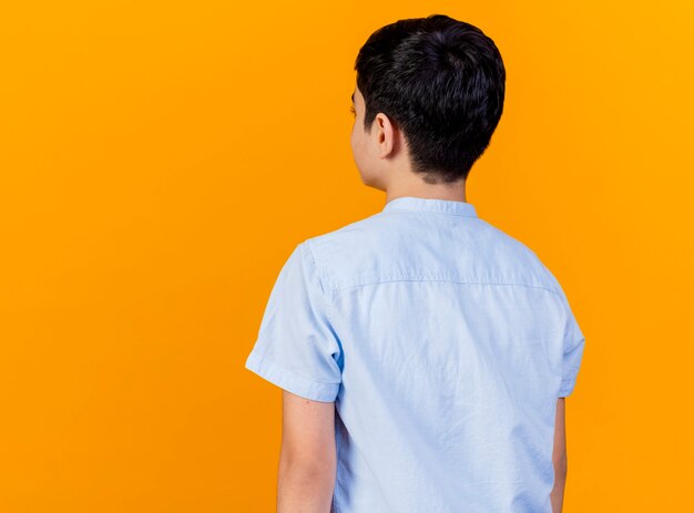 Young caucasian boy standing in behind view isolated on orange background with copy space