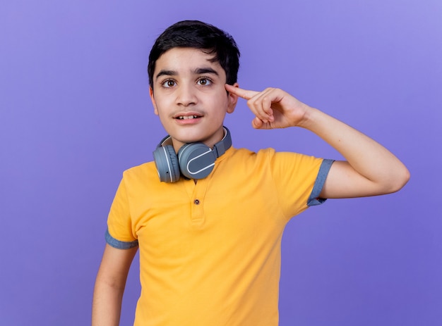 Young caucasian boy wearing headphones on neck isolated on purple wall