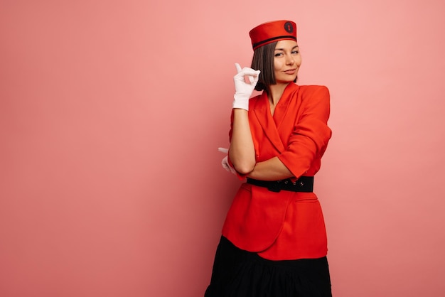 Young caucasian brunette in red jacket looks thoughtfully into camera pointing her finger at empty pink space Advertising concept