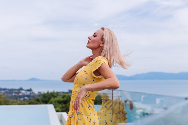 Young caucasian calm happy pretty woman with bright evening makeup wearing summer yellow dress and sea shell necklace