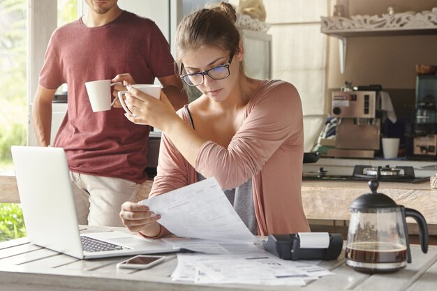 Young Caucasian family calculating bills, reviewing finances and planning family budget together in kitchen