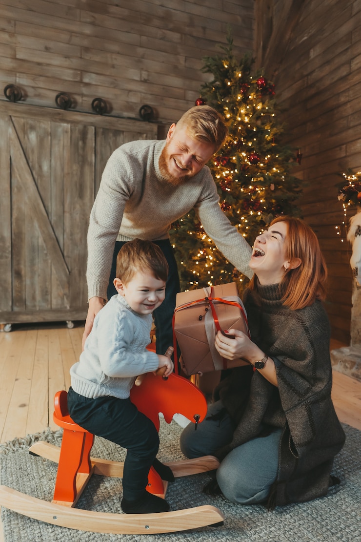 Free Photo young caucasian family mom dad son near fireplace christmas tree