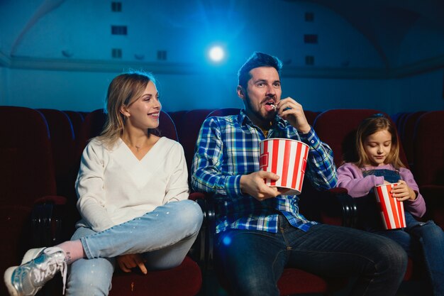 Young caucasian family watching a film at a movie theater, house or cinema. Look expressive, astonished and emotional. Sitting alone and having fun. Relation, love, family, childhood, weekend time.