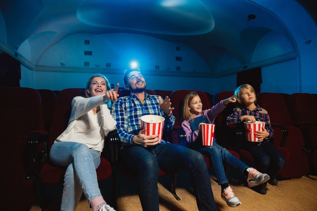 映画館、家または映画館で映画を見ている若い白人家族。表現力豊かで、驚いて、感情的に見えます。一人で座って楽しんでください。関係、愛、家族、子供時代、週末の時間。