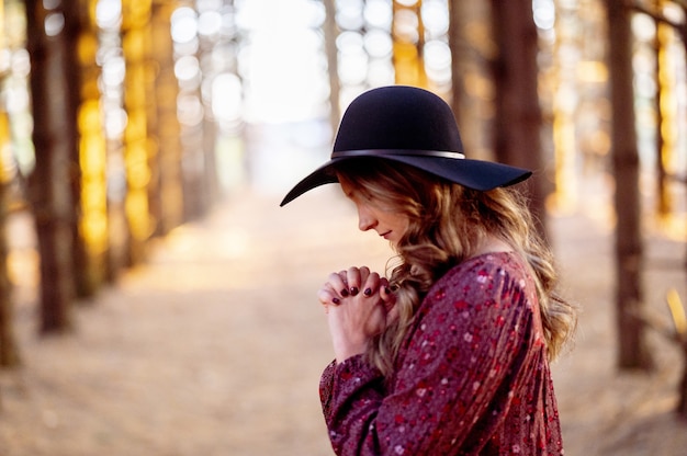 風光明媚な森、秋の気分で祈るスタイリッシュな黒い帽子をかぶった若い白人女性
