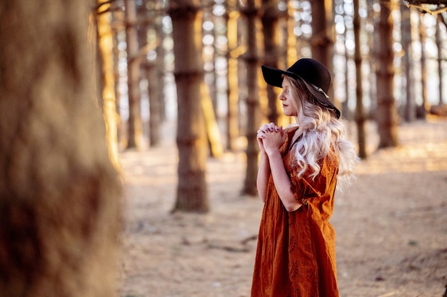 아름다운 숲에서 기도하는 세련된 검은 모자를 쓴 젊은 백인 여성, 가을 분위기