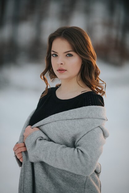 Young Caucasian female wearing a gray coat posing in a winter park covered in snow