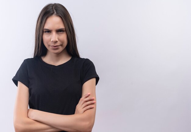 молодая кавказская девушка в черной футболке, скрестив руки на изолированной белой стене