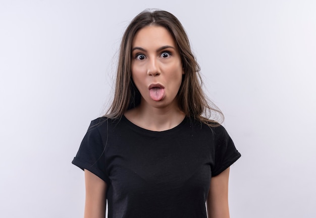 молодая кавказская девушка в черной футболке показывает язык на изолированной белой стене