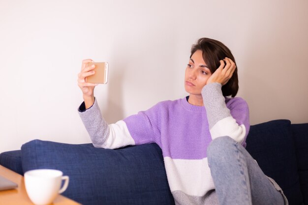 ソファの上の寝室で若い白人の女の子の女性は携帯電話のカメラを見てください