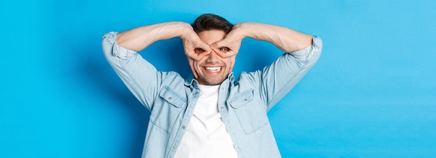 Free photo young caucasian guy showing funny expression making superhero mask with fingers on eyes smiling happ