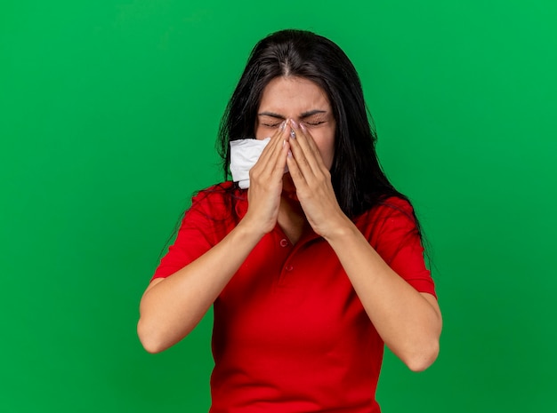 Foto gratuita tovagliolo della holding della giovane ragazza malata caucasica che tiene le mani sul naso che starnutisce isolato sulla parete verde con lo spazio della copia