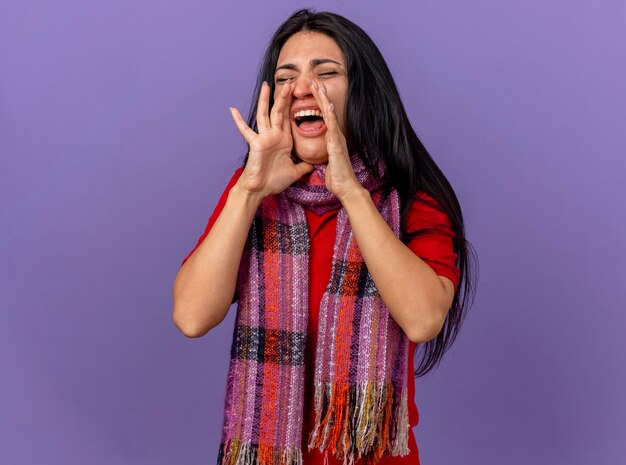 Young caucasian ill girl wearing scarf keeping hands near mouth calling out loud to someone with closed eyes isolated on purple wall with copy space