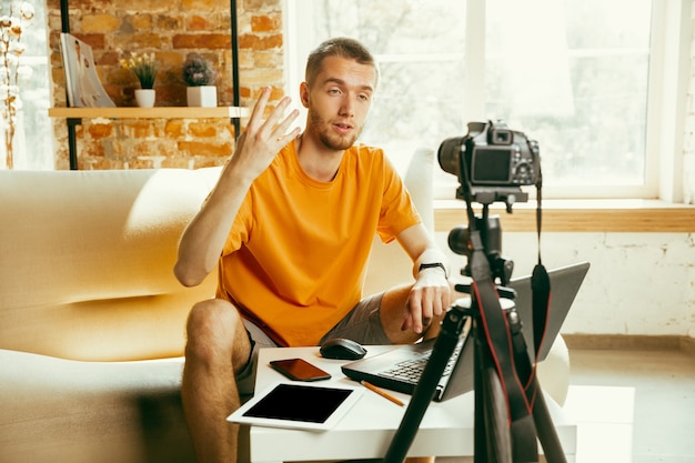 Young caucasian male blogger with professional camera recording video review of gadgets at home. Blogging, videoblog, vlogging. Man making vlog or live stream about photo or technical novelty.