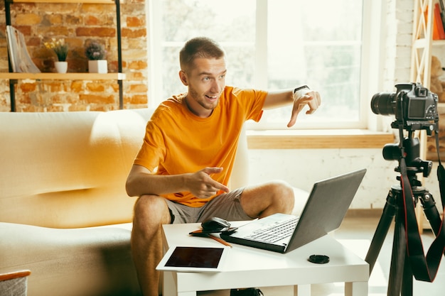 Young caucasian male blogger with professional camera recording video review of gadgets at home