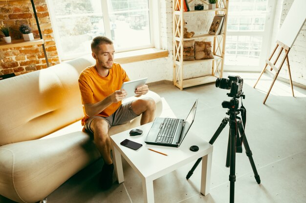 Молодой кавказский блоггер-мужчина с профессиональной камерой, записывающей видеообзор планшета дома