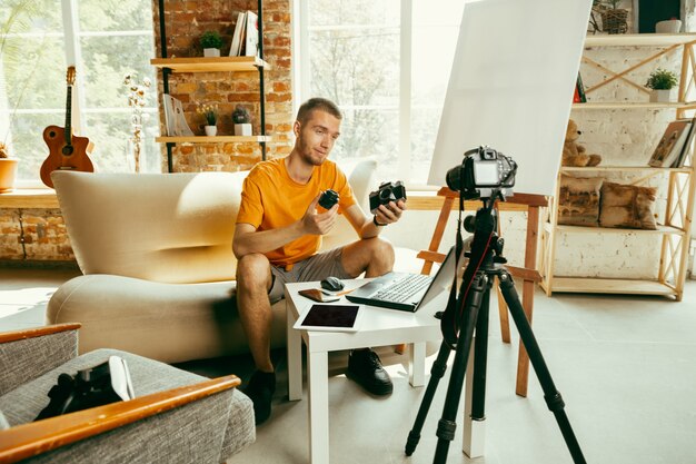 Молодой кавказский блоггер мужского пола с профессиональным оборудованием, записывающим видеообзор камеры дома. Блог, видеоблог, видеоблог. Мужчина ведет видеоблог или прямую трансляцию о фото или технических новинках.