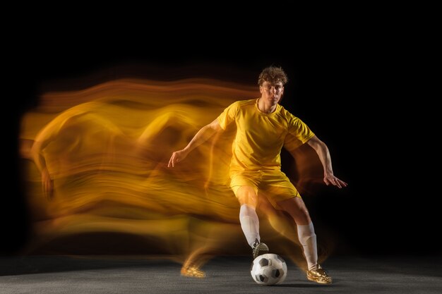 Free photo young caucasian male football or soccer player kicking ball for the goal in mixed light on dark wall concept of healthy lifestyle professional sport hobby