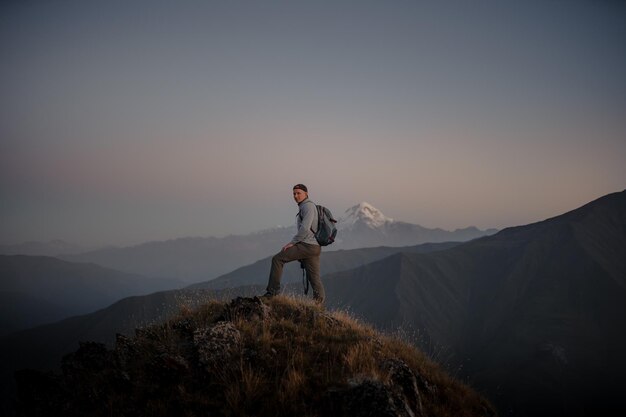 Young Caucasian male hiker standing at the top of a grassy mountain and admiring the foggy nature