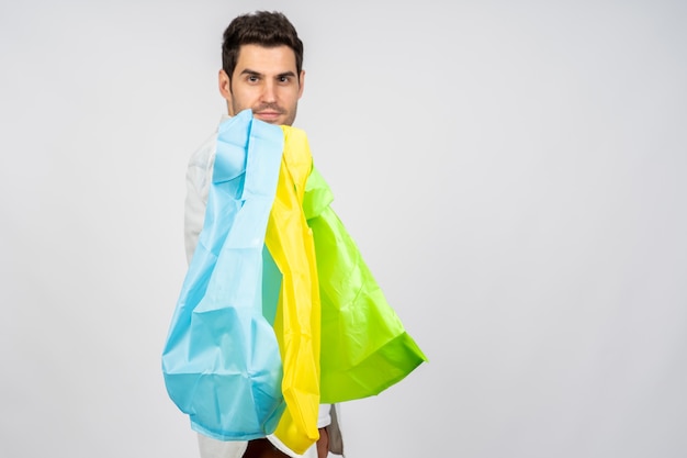 Young Caucasian male holding reusable shopping bags against a white wall