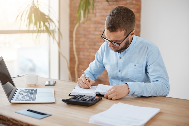 Free photo young caucasian male manager in glasses sitting in company office