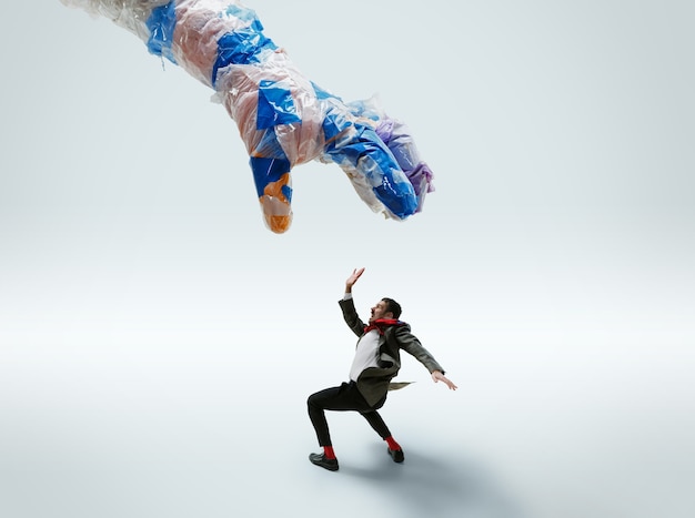 Young caucasian man avoiding big plastic hand on white  background.
