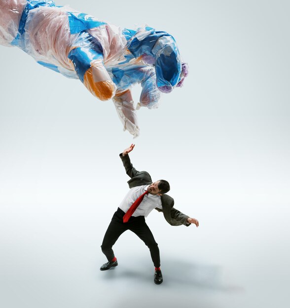 Young caucasian man avoiding big plastic hand on white  background.