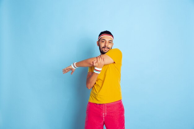 Young caucasian man in bright clothes training on blue background Concept of sport, human emotions, facial expression, healthy lifestyle, youth, sales. Doing stretching exercises. Copyspace.