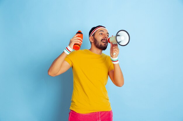 Young caucasian man in bright clothes training on blue space Concept of sport, human emotions, facial expression, healthy lifestyle, youth, sales