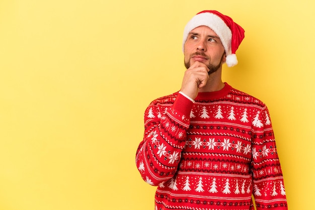 疑わしいと懐疑的な表情で横向きに見える黄色の背景に分離されたクリスマスを祝う若い白人男性。