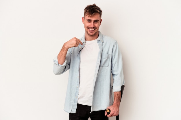 Young caucasian man holding crutch isolated on white background person pointing by hand to a shirt copy space, proud and confident