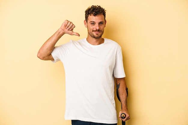 Young caucasian man holding crutch isolated on yellow background feels proud and self confident, example to follow.