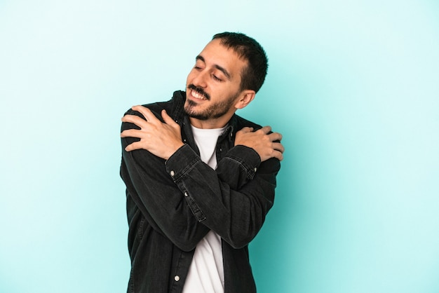Young caucasian man isolated on blue background hugs, smiling carefree and happy.