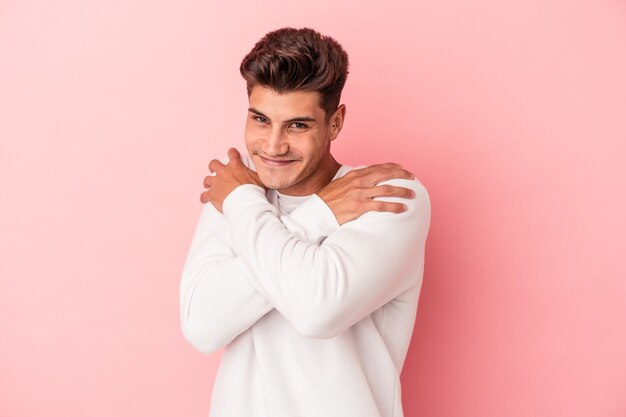 Young caucasian man isolated on pink background hugs, smiling carefree and happy.
