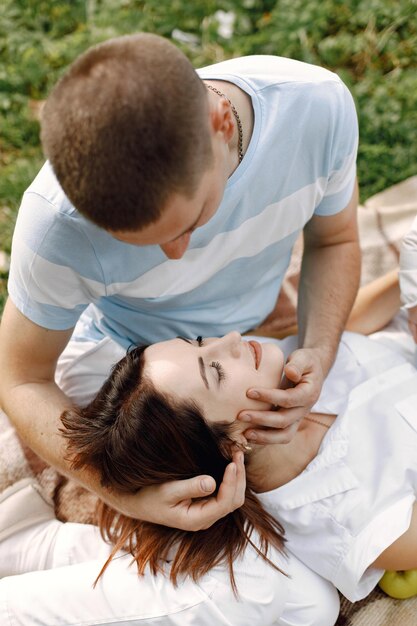 Young caucasian man in love looking at his wife resting her head on his laps when they are having picnic in park Man and woman relaxing in a park Brunette woman wearing white