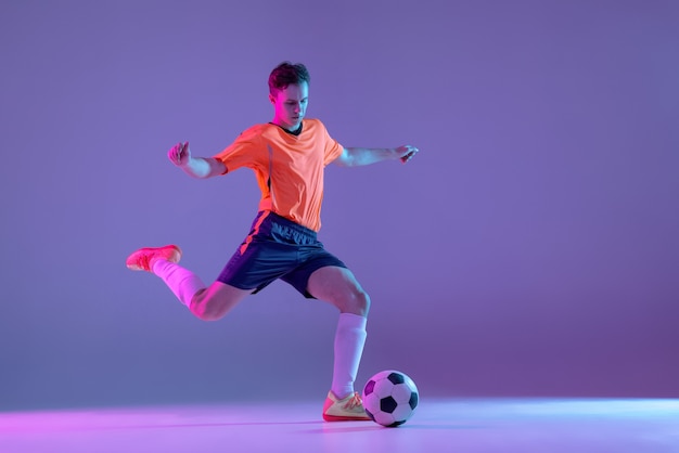 Young caucasian man male soccer football player training isolated on gradient blue pink wall in neon light