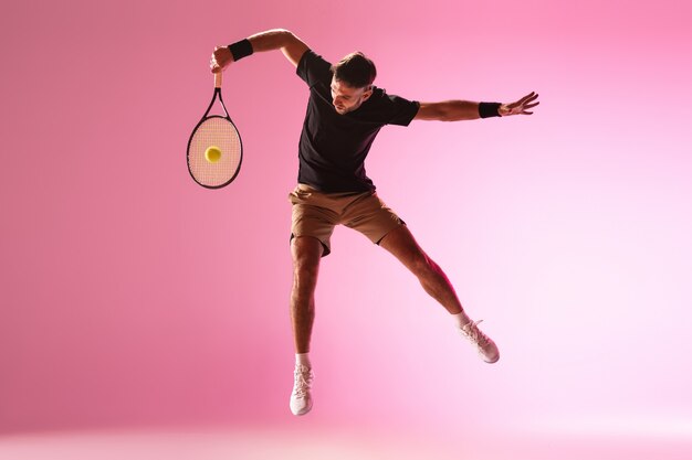 Young caucasian man playing tennis isolated on pink  wall action and motion concept