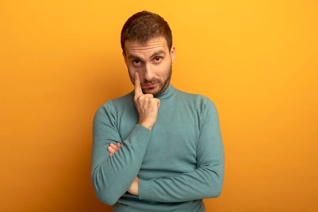 Young caucasian man  pulling eye lid down isolated on orange wall with copy space