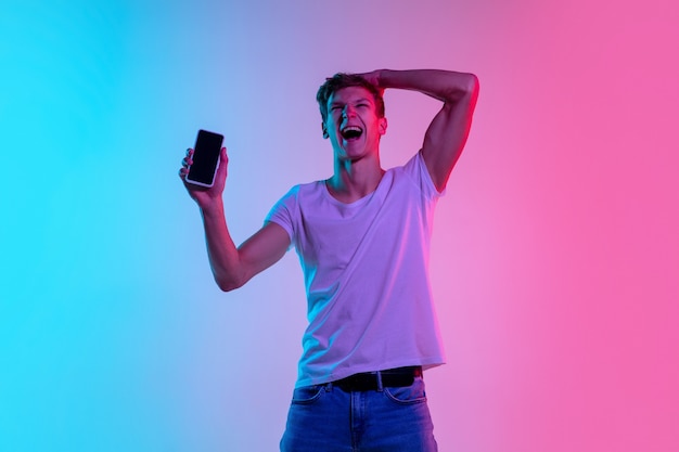 Young caucasian man's jumping high on gradient blue-pink studio in neon light