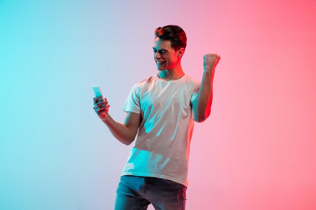 Young caucasian man's portrait on gradient blue-pink studio in neon light