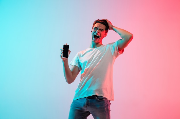 Young caucasian man's portrait on gradient blue-pink studio in neon light