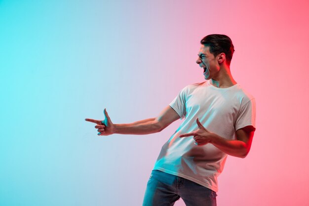 Young caucasian man's portrait on gradient blue-pink studio in neon light