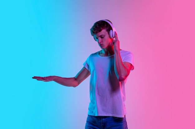 Young caucasian man's portrait on gradient blue-pink studio in neon light