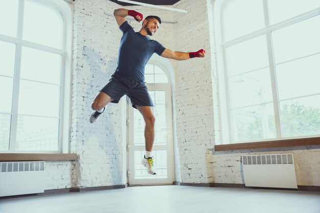 Young caucasian man training at home during recording online courses, doinc exercises of fitness, aerobic. Staying sportive suring insulation.