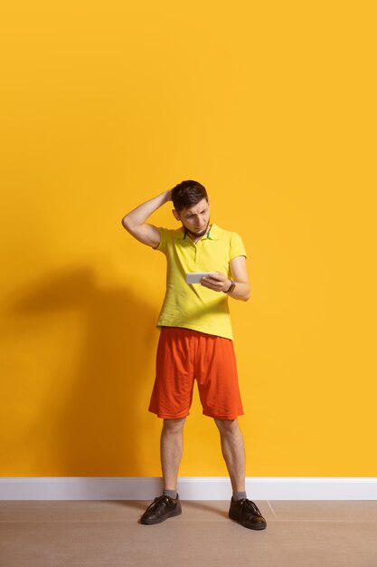 Young caucasian man using smartphone full body length portrait isolated over yellow wall