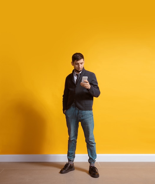 Young caucasian man using smartphone full body length portrait isolated over yellow wall