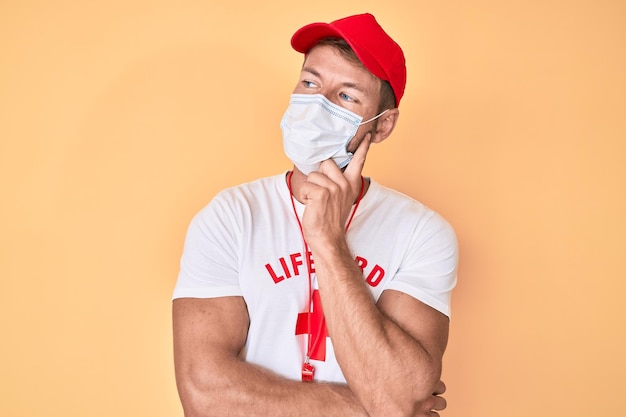 Free photo young caucasian man wearing lifeguard t shirt using medical mask serious face thinking about question with hand on chin thoughtful about confusing idea