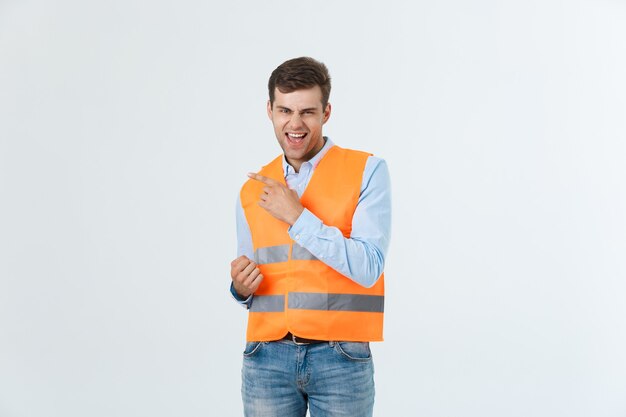 Молодой кавказский человек на белом фоне, одетый в форму подрядчика и защитный шлем, удивлен идеей или вопросом, указывая пальцем со счастливым лицом, номер один.
