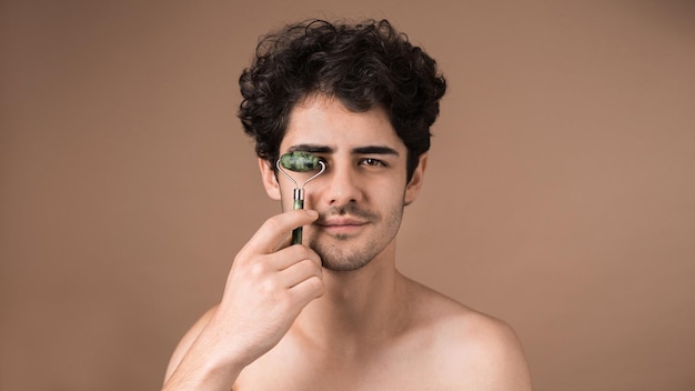 Un giovane uomo caucasico con la barba ispida sta facendo un massaggio facciale usando un rullo